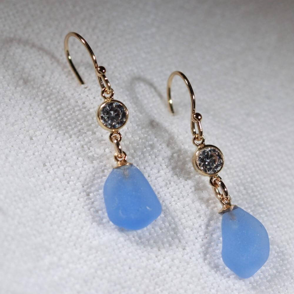 Cornflower Sea Glass Earrings in 14 kt gold-filled hanging from a sparkly bezel set CZ